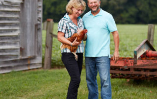 Michael and Amy Drewry standing outdoors holding one of their chickens